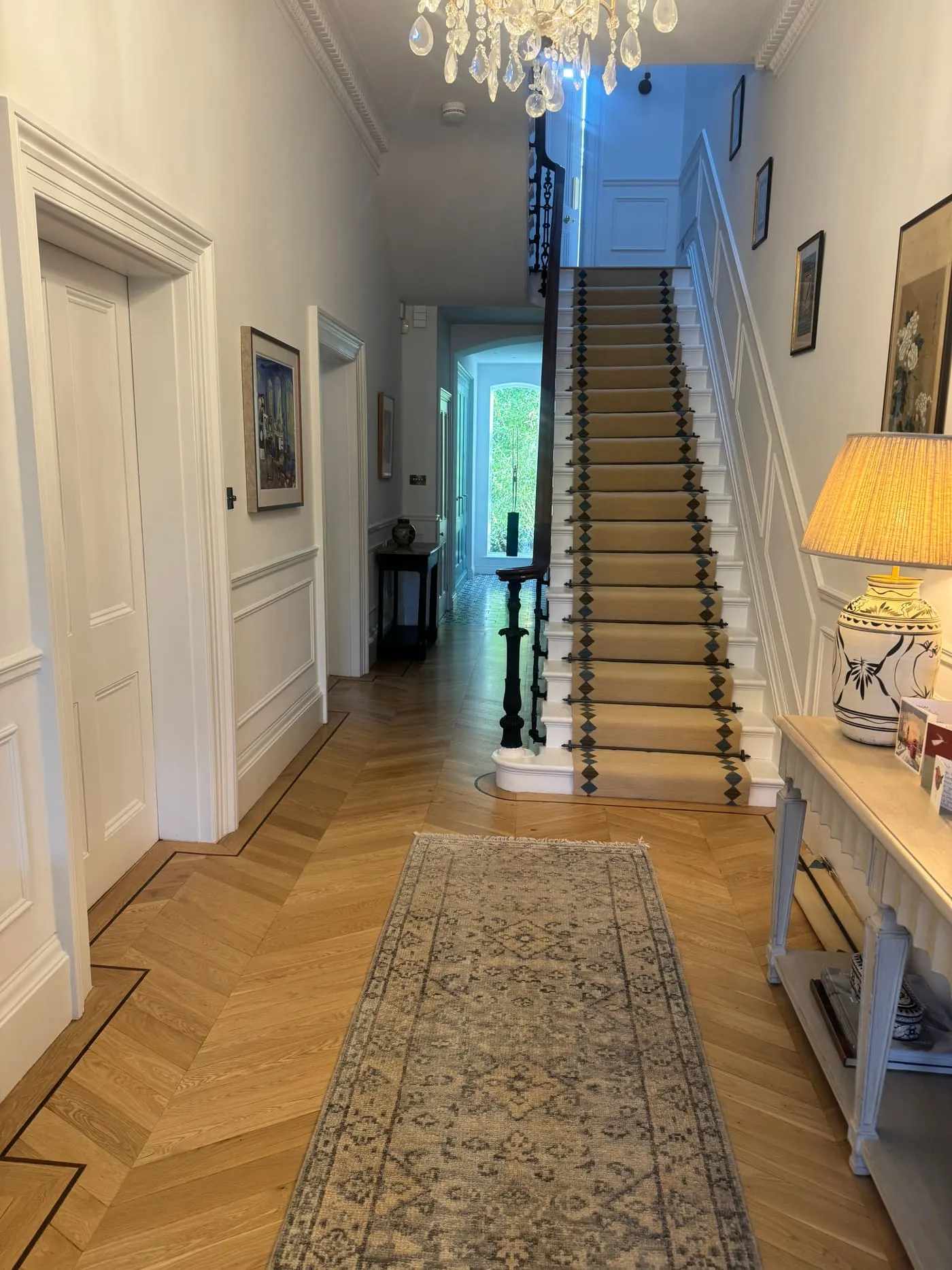 Herringbone parquet hallway with a patterned stair runner leading upstairs